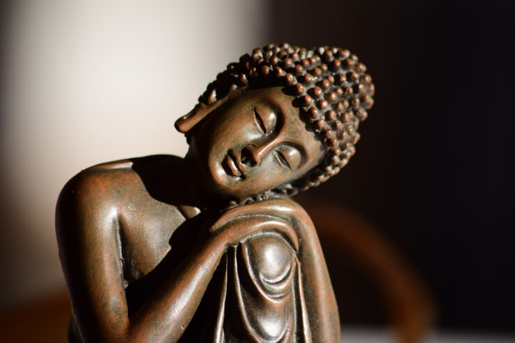 buddah figur mit kopf auf dem knie vor dunkelbraunem hintergrund