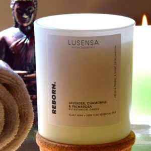 lusensa-duftkerze-reborn-mood Bild mit einer Duftkerze im Glas, eine brennende Kerze und einer Buddha-Figur im Hintergrund