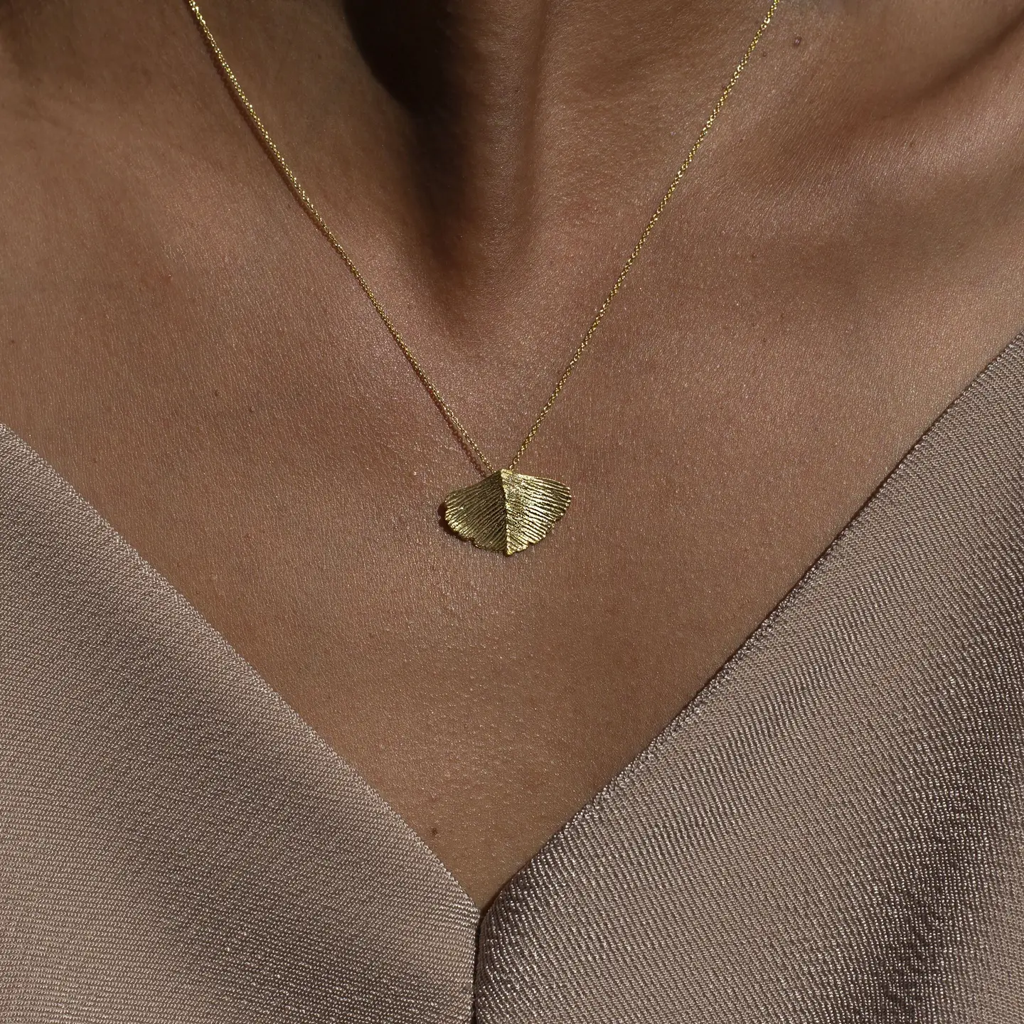 seelenanker-halskette-gingko-blatt Frau, die eine goldene Halskette mit Gingkoblatt Anhänger trägt